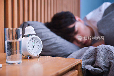 Sleepy asian man turning off alarm clock in bed